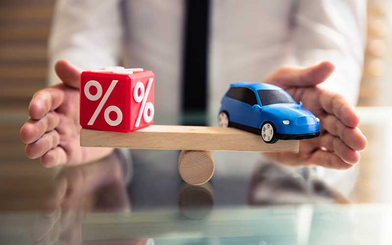 Hands balancing a red percent cube and a blue toy car on a seesaw